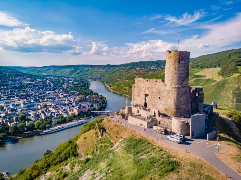 Die Burg Landshut thront über der Mosel und der Doppelstadt Bernkastel-Kues. Im Hintergrund erheben sich Hügel. 