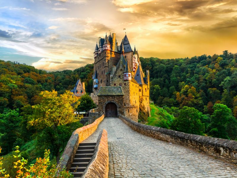 Burg Eltz mit hohen Türmen, Erkern und Fachwerk-Verzierungen inmitten des Waldes bei bewölktem Himmel. 