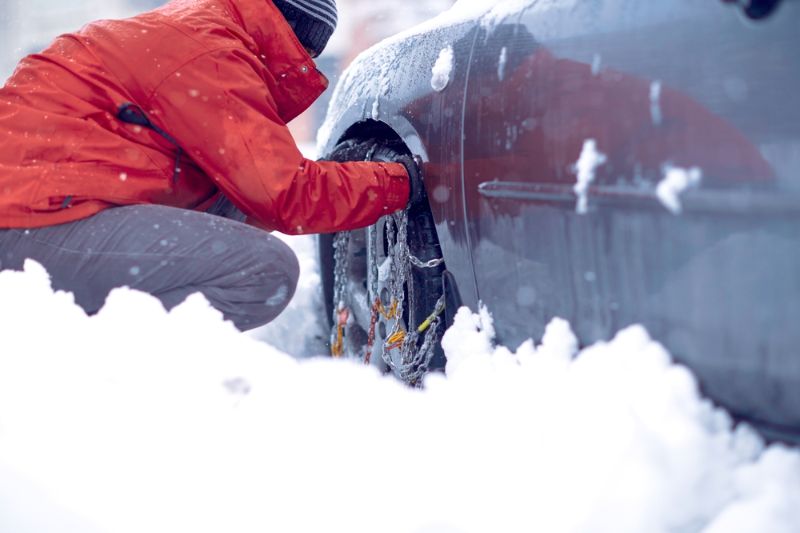 Mann bringt Schneeketten auf dem Vorderrad des Autos an.