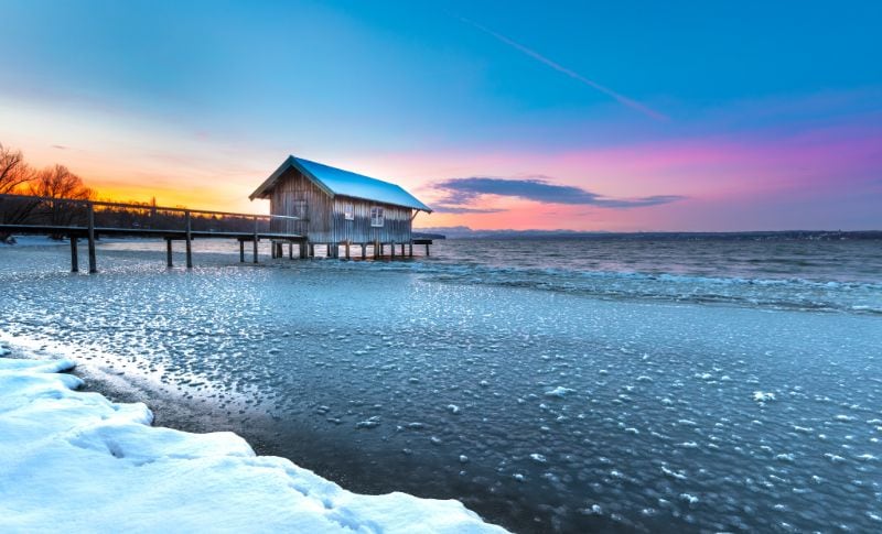 Altes Seehäuschen im Ammersee im Winter und mit gefrorener Eisfläche im Uferbereich